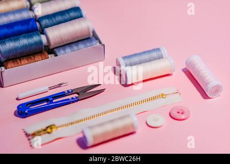 Cucitura piatto posare. Vista dall'alto degli accessori da cucire su sfondo rosa: Pinze, zip, bottoni e fili da cucire. Industria di dressmaaking e artigianato Foto Stock