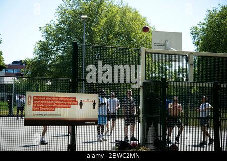 Hackney, Londra, maggio 2020 durante la pandemia di Covid-19 (Coronavirus). Un gruppo di giovani uomini gioca a basket ignorando le regole di allontanamento sociale. Foto Stock