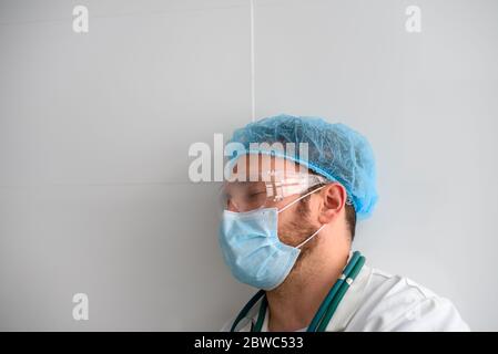 Medico esausto in ospedale con occhi chiusi in maschera facciale Foto Stock