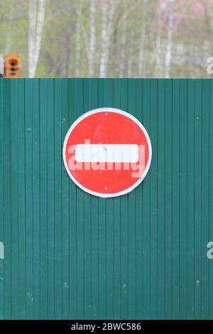 Cartello rosso rotondo con striscia bianca che impedisce il movimento sulla recinzione verde di lamiera. Non entrare. Concetto di divieto, di fine cieco, disperazione e stop. Foto Stock