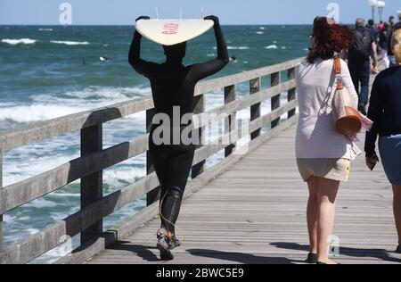 Binz, Germania. 31 maggio 2020. Una donna sta portando una tavola da surf sul molo accanto ai passanti, camminando attraverso il molo. Il vivace vento del nord-est ha portato gioia a surfisti e kite surfisti. Vicino al molo i surfisti stavano aspettando le onde più alte. Escursionisti e bagnanti popolarono anche la spiaggia, che era diventata stretta a causa del vento onshore, a temperature intorno ai 15 gradi. Credit: Stefan Sauer/dpa-Zentralbild/dpa/Alamy Live News Foto Stock