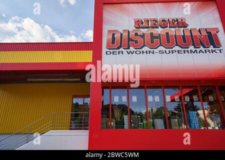 Germania - 21 maggio 2020: Rieger Sconto immediatamente ed economico, giallo rosso facciata con pubblicità, vetri riflettenti. Cielo blu nuvoloso Goeppingen. Foto Stock