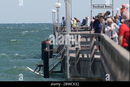 Binz, Germania. 31 maggio 2020. I turisti camminano sopra il molo mentre un surfer lascia la sua tavola nell'acqua. I venti vivaci del nord-est hanno portato gioia ai surfisti e ai kite surfisti. Vicino al molo i surfisti aspettavano le onde più alte. Escursionisti e bagnanti popolarono anche la spiaggia, che era diventata stretta a causa del vento onshore, a temperature intorno ai 15 gradi. Credit: Stefan Sauer/dpa-Zentralbild/dpa/Alamy Live News Foto Stock