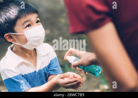 Madre prendersi cura figlio con maschera viso e disinfettante per la protezione malattia influenza o covid-19 all'aperto, mamma e bambino indossare maschera medica mano pulita per s. Foto Stock