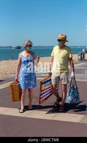 Southsea, Portsmouth, Inghilterra, Regno Unito. Maggio 2020. Coppie anziane che indossano maschere mediche che trasportano l'attrezzatura da picnic sulla passeggiata a Southsea, Regno Unito. Foto Stock