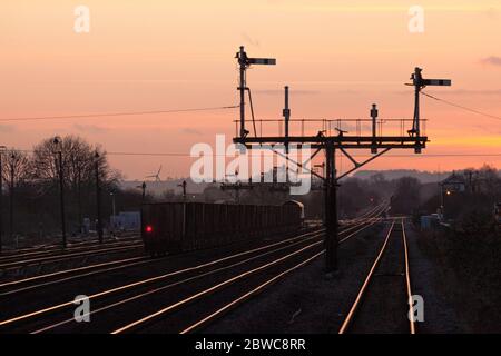 DB Cargo Rail locomotiva UK classe 66 66161 trasporto di un treno merci che trasporta minerale di ferro che passa i segnali semaforici a Barnetby, Lincs, al tramonto Foto Stock