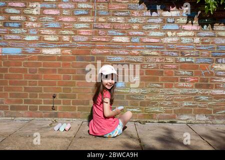 Giovane ragazza felice colorazione in mattoni casa con gesso pastelli, UK Foto Stock