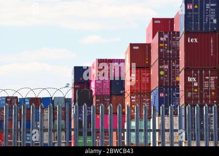 I container per il trasporto merci sono impilati dietro una recinzione sormontata da filo spinato in uno dei porti più trafficati del Regno Unito Foto Stock