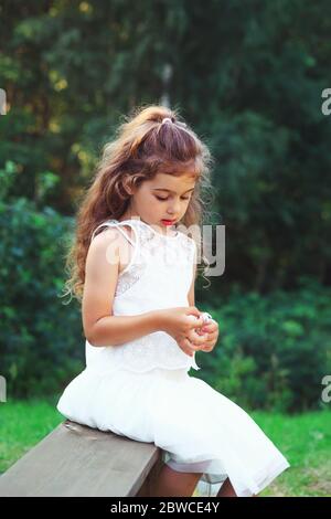 Bella bambina che gioca con i fiori nel parco primaverile. Felice bambino carino divertirsi all'aperto al tramonto. Foto Stock