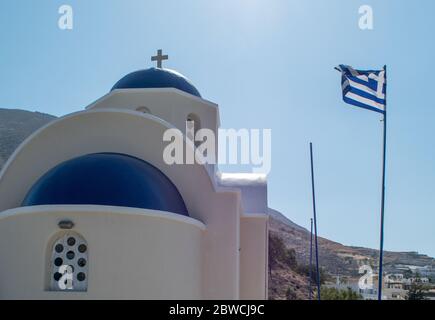 Angolo di una tradizionale chiesa ortodossa greca di colore blu e bianco con una croce in alto e la bandiera greca che svetta a destra Foto Stock