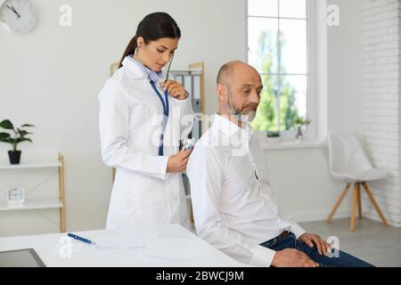 Una dottoressa con stetoscopio fa una diagnosi ad un anziano pensionato paziente in un moderno ufficio ospedaliero. Foto Stock