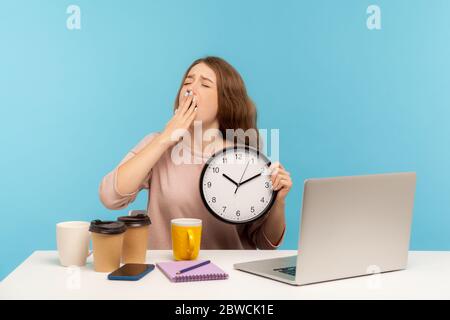 Stanco dipendente dell'ufficio che lavora in tarda ora. Donna esausta circondata da tazze di caffè che brilitano e tengono orologio, sensazione di fatica, stress di lavoro straordinario Foto Stock