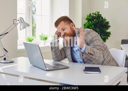 Videochiamata con chat online. Uomo d'affari positivo che effettua videochiamata tramite laptop e mano sventolante. Foto Stock