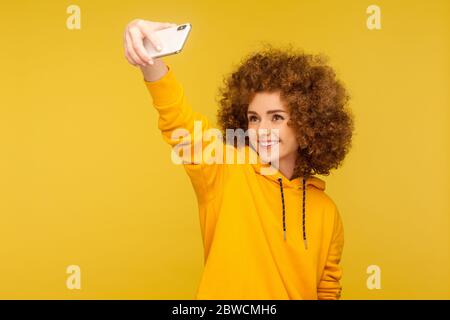 Ritratto di bella donna trendy capelli ricci in stile urbano felpa di presa selfie, avendo conversazione su videochiamata o blog in streaming, trasmissione. io Foto Stock