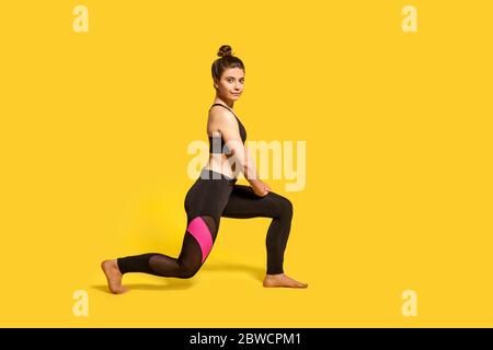 Giovane donna atletica sottile con capelli in pezza sport fare sport affondo esercizio, in piedi un ginocchio, riscaldamento muscoli di allenamento, glutine allenamento. Foto Stock