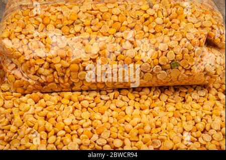 Piselli spezzati gialli in un sacchetto di plastica e cereali sfusi su uno sfondo di tela con una consistenza ruvida. Cereali tradizionali per la preparazione di zuppe e porridg Foto Stock