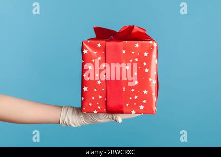 Profilo Vista laterale primo piano della mano umana in guanti chirurgici bianchi che tengono una confezione regalo rossa. Concetto di condivisione, donazione o consegna. Interno, studio shot, isola Foto Stock