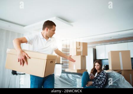 Concetto di movimento e di relazione. Non è soddisfatto. Il marito disimballa le scatole. E la moglie nel frattempo non fa nulla. Preferisce parlare con lei Foto Stock