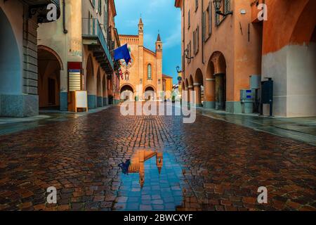 Piccolo dazzolo su una stretta strada acciottolata tra vecchie case e la cattedrale di San Lorenzo sullo sfondo della città di Alba, Piemonte, Italia settentrionale. Foto Stock