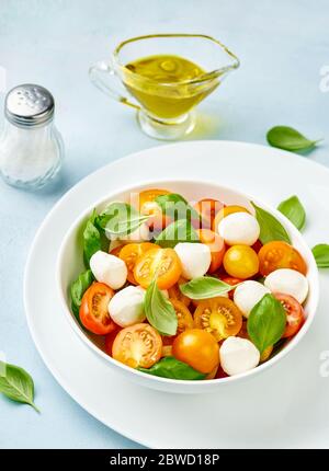 Insalata caprese con ciliegia di pomodoro gialla e mini mozzarella in ciotola bianca su piatto bianco. Mozzarella di bocconcini con foglie di basilico. Foto Stock