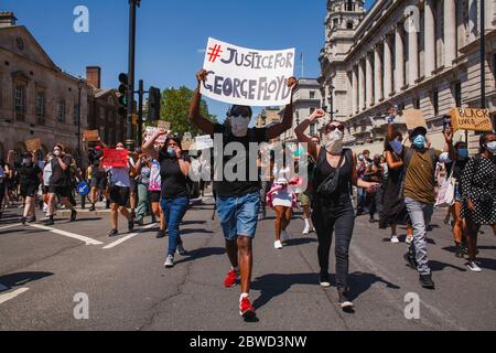 Gli attivisti marciano lungo Whitehall mentre tengono cartelli durante la dimostrazione George Floyd. Migliaia di persone si sono riunite per la protesta, nonostante le continue preoccupazioni per la possibile diffusione del coronavirus e le continue richieste delle autorità di rispettare le linee guida per le distanze sociali. Floyd, un uomo nero, morì come ufficiale di polizia bianca, Derek Chauvin, inginocchiato al collo durante un arresto nella città americana di Minneapolis il 25 maggio. La morte di Floyd, che ricorda la morte di Eric Garner per mano di agenti di polizia a New York nel 2014, ha riacceso l'agai del movimento 'Black Lives Matter' Foto Stock