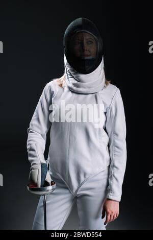 Fencer in maschera scherma e pinza di tenuta tuta isolato su nero Foto Stock