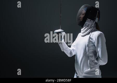 Vista laterale del fencer nella maschera di recinzione che tiene la pinza isolata su nero Foto Stock