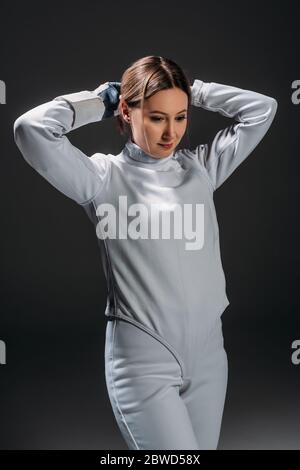 Fencer in tuta scherma che intreccia i capelli isolati su nero Foto Stock