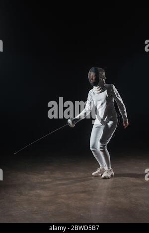 Spada in tuta da scherma e maschera con pinza su sfondo nero Foto Stock