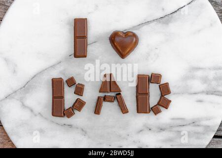 Festeggiando il giorno del Padre o il compleanno. Frase Io amo papà disposto in lettere di cioccolato su un vassoio di marmo Foto Stock