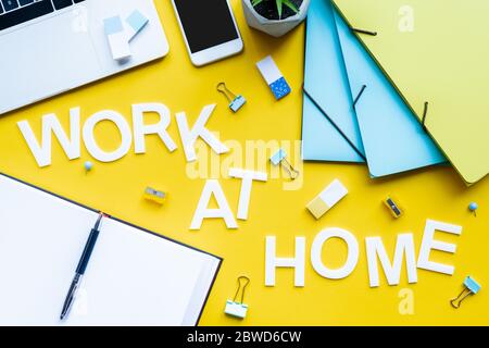 Vista dall'alto della scritta lavoro a casa vicino al notebook aperto e della cancelleria su sfondo giallo Foto Stock