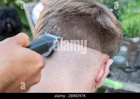 Un uomo tenta di tagliare i capelli di un altro uomo durante il blocco del coronavirus quando i parrucchieri sono chiusi, lasciando la coda di un ratto giù un lato della testa Foto Stock