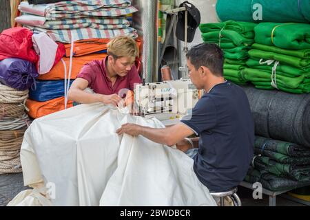 Ho Chi Minh City, Vietnam - 11 febbraio 2019: Gli uomini vietnamiti cuciscono un tessuto con una macchina da cucire nella strada vicino al loro piccolo negozio. Foto Stock