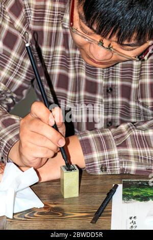 Wang Zhen, un incisore maestro, mostra agli studenti come tagliare un sigillo o un foca alla società dell'incisore Xiling Seal di Hangzhou, Cina. Inizialmente ci erano le foche Foto Stock