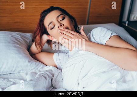 bella ragazza che brilita mentre si sdraia a letto al mattino durante la quarantena Foto Stock