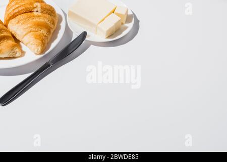 gustosi croissant appena sfornati sul piatto vicino al burro con coltello su sfondo bianco Foto Stock