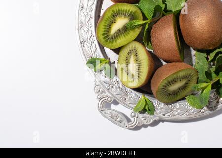 vista dall'alto di gustosi kiwi vicino alla menta fresca su un piatto argentato isolato su bianco Foto Stock