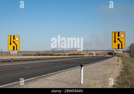 vista di un gran numero di segnali di avvertenza per la riparazione stradale su una strada statale su una nuova superficie asfaltata in una zona collinare Foto Stock