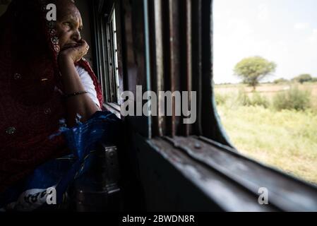 Donna che guarda fuori dalla finestra del treno mobile, treno di seconda classe. Ferrovie indiane. India. Foto Stock