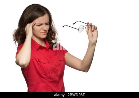 Bella ragazza giovane in una camicia rossa su uno sfondo bianco che ha occhi irritati e una testa da occhiali Foto Stock