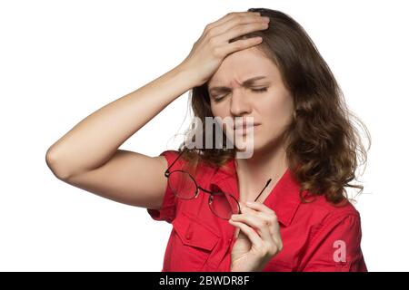 Bella ragazza giovane in una camicia rossa su uno sfondo bianco che ha occhi irritati e una testa da occhiali Foto Stock