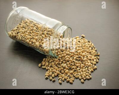 Essiccato black eyed peas o fagioli (Vigna unguiculata o cowpea sono versato da un barattolo di vetro marrone sulla superficie di legno. cowpea in un vasetto di vetro sul legno t Foto Stock