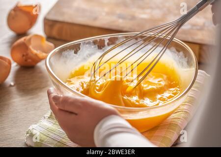 Dettaglio delle uova che vengono mescolate in una ciotola posta su un asciugamano e un tavolo di legno Foto Stock