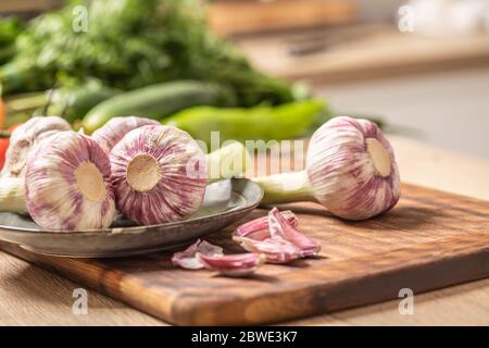 Cinque teste di aglio su un tagliere con verdure verdi sullo sfondo Foto Stock