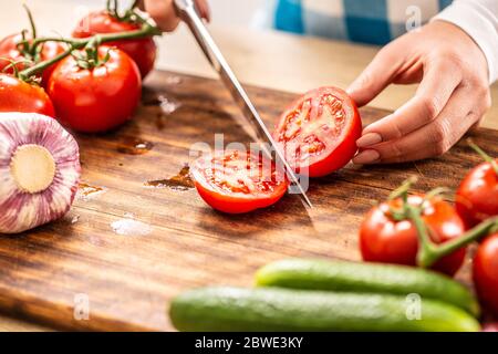 Dettaglio di un pomodoro tagliato a metà su un tagliere con cetriolo, aglio e più pomodori da parte Foto Stock