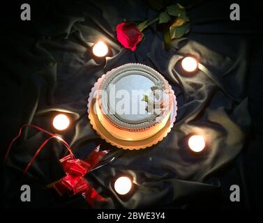 Torta di nozze decorata per un appuntamento romantico. Design incantevole per una notte romantica. Torta intorno: Candele, coltello decorato, rosa fiore rosso. Foto Stock