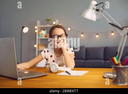 Formazione scolastica online. La ragazza felice intelligente in occhiali sorride insegna una lezione utilizzando un computer portatile in camera. Foto Stock