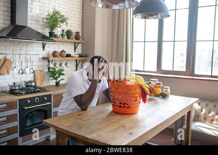 Uomo afro-americano seduto al cesto con vestiti e stanco Foto Stock