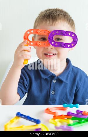 Adorabile ragazzo fatto bicchieri di plastica a blocchi giocattolo e sorridente. Foto verticale di divertente bimbo Foto Stock