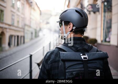 Vista posteriore del corriere con zaino e casco da bicicletta in città. Foto Stock